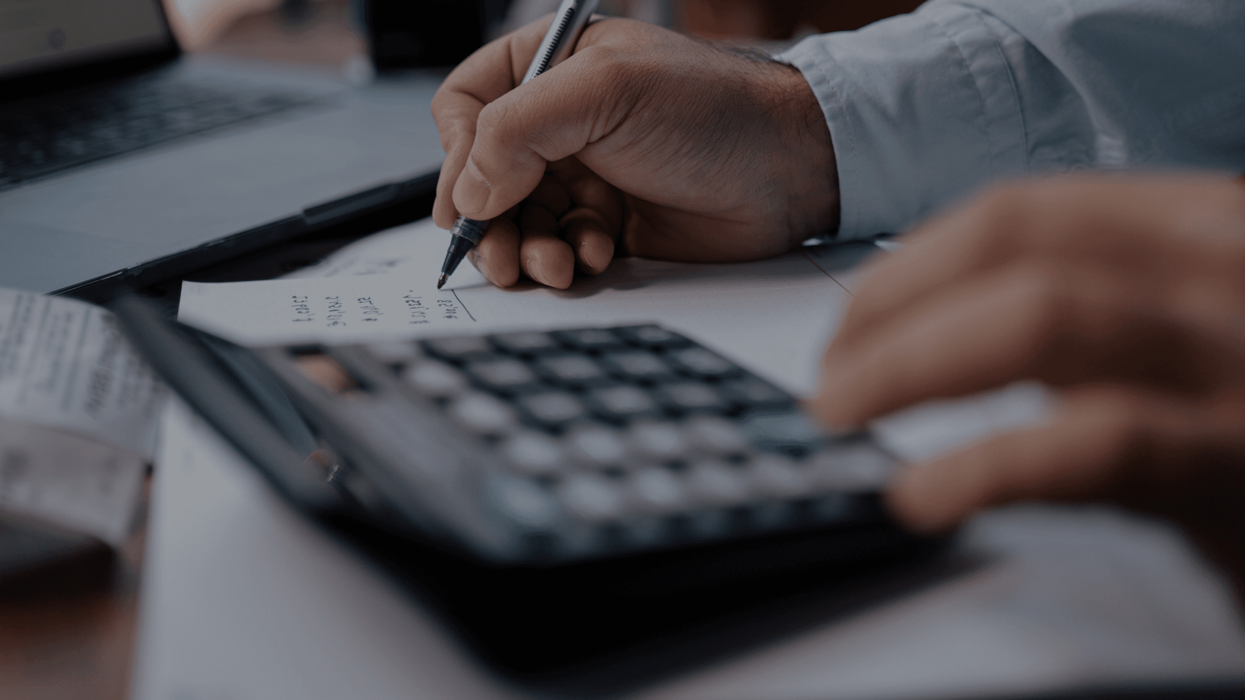 Hands using a calculator and writing financial notes